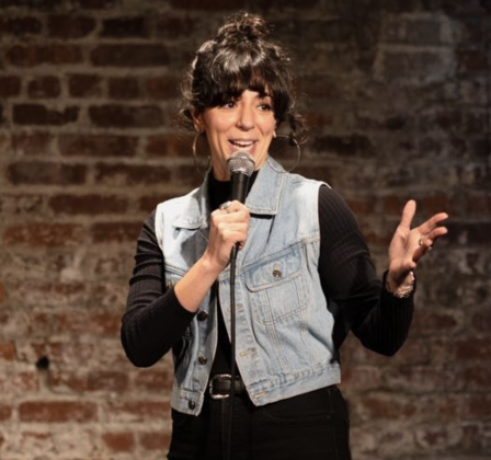 Alex Kumin performing stand-up comedy live on stage at a New York City comedy club.
