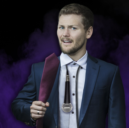 Drew Lynch holding a tie with a microphone around his neck, wearing a suit on a purple smoky background – NYC comedy show promotion